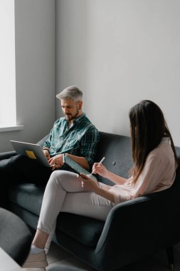 Kanepede oturan bir adam ve bir kadın dizüstü bilgisayar ve tabletle çalışıyorlar.