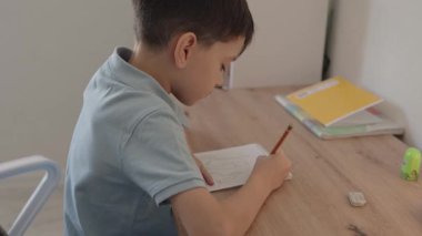 Genç bir çocuk masasında oturuyor, defterine derin bir şekilde çizim yapıyor. Sahne yaratıcılık, huzur ve çocukluk merakını çağrıştırıyor..