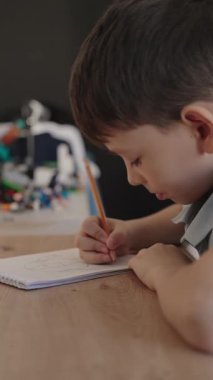 Odaklanmış genç bir çocuk kalemle bir not defteri çizer, sanat yoluyla yaratıcılık ve hayal gücünü ifade eder. Bu iç açıcı sahne çocukluk masumiyetini ve yaratılış sevincini yakalar..