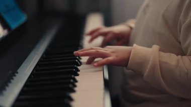 Dijital piyano çalan bir çocuğun ellerinin yakın çekimi. Çocuk müzik dünyasını öğreniyor ve keşfediyor..