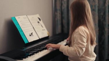 Genç bir kız piyanosunun başına oturmuş, müzik çalışıyor. Notaları okuyup tuşları çalarken odaklanmış ve kararlı..