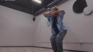 Dinamik bir kadın dansçı geniş bir dans stüdyosunda güçlü ve sanatsal hareketler sergiliyor..