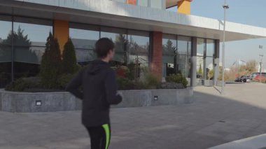 A young man in athletic wear jogs through a contemporary urban landscape, emphasizing fitness and well-being.