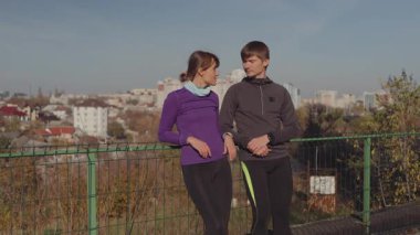 Young athletic couple taking a break from their run, conversing in an urban park on a sunny day.