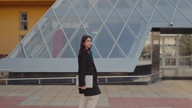 Profesyonel bir kadın, şehir ortamında dizüstü bilgisayarıyla, modern iş ve kariyerini yansıtarak güvenle yürür..