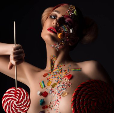 Genç güzel kız bebek gibi lolipop onun el ve tüm onun yüz ve siyah arka plan üzerine sanatsal portre kırpılmış meme karamel saç modeli ile.