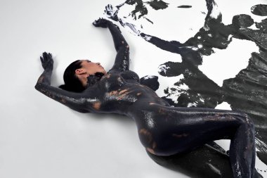 Tüm vücudu siyah yağlı boyayla boyanmış çıplak bir kadın. Beyaz ovada yalanlar ve erotik danslar yapıyor. Koyu renk boyayla.