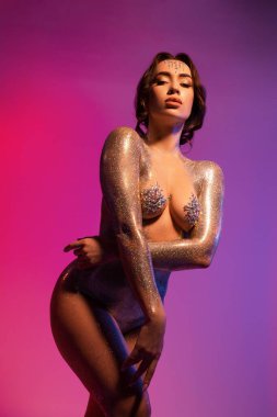 Kendine güvenen genç, zinde, çıplak vücudunda parlak gümüş boyası olan ve kameraya bakan bir model.