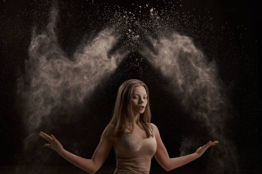 İç çamaşırı giymiş, gözlerini kapayan, koyu arkaplanda tozu sıçratan bir sürü çıplak genç kadın.