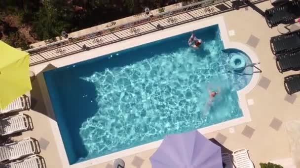 晴れた日にクロアチアの道路近くのリゾートでプールで泳ぐ母と2人の子供のトップビュー — ストック動画