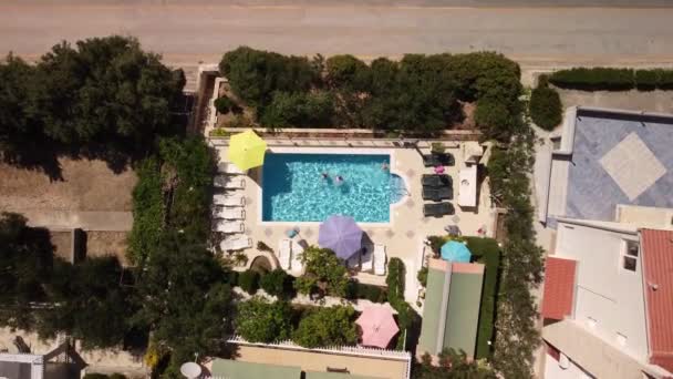 サンベッドと傘のあるホテルでの青いスイミングプールのトップビュー夏の日の道路に近い — ストック動画
