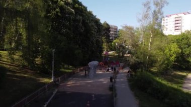 Güneşli bir günde yeşil parktaki çocuk ve yetişkinlerle dolu salıncaklı ve atlı karınca manzaralı uzun oyun parkları.