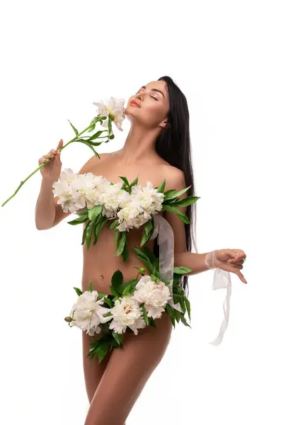 自己は新鮮な繊細な花束のボディをカバーし 白い背景に対してカメラを見る長い暗い髪の若い裸の女性モデルを保証しました ストック写真
