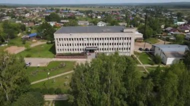 Yazın güneşli bir günde yeşil ağaçlar ve çimlerle çevrili büyük beton okulun havadan görünüşü