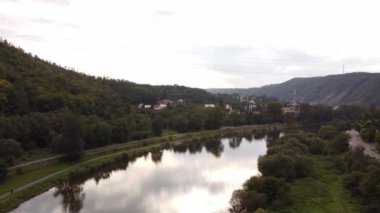 Bulutlu bir günde yeşil ağaçlar ve dağlarla çevrili sakin nehrin insansız hava aracı görüntüsü, Vrane nad Vltavou