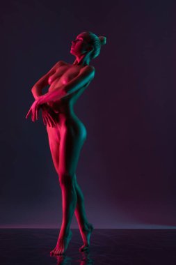 Genç çıplak kadın modelinin tüm vücudu koyu arkaplanda duran ışık renginde.