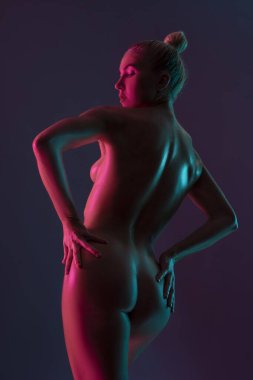 Arka planda profilde, sarışın, kolları kalçasında, koyu mor arka planı ise sarı çizilmiş genç bir kadın var.