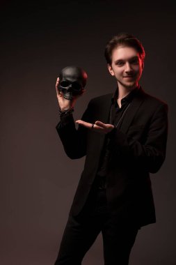 Siyah elbiseli kendinden emin genç adam gülümsüyor ellerinde kafatası