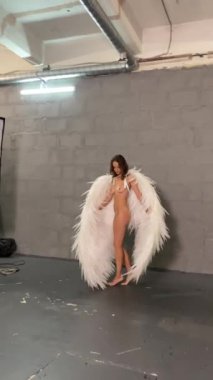 Melek kanatlı bir model stüdyo ortamında poz veriyor. Sırtı kameraya dönük duruyor..