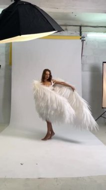 Stüdyoda bir kadın büyük, beyaz melek kanatlarıyla poz veriyor..