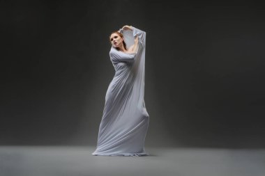 Bir dansçı zarif bir şekilde akıcı bir elbiseyle hareket eder. Zarif bir zarafet ve loş bir mekanda duruş sergiler..