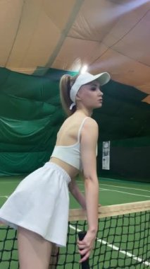 Genç bir kadın tenis antrenmanı sırasında geniş bir iç saha sahasında hizmet vermeye hazırlanıyor..