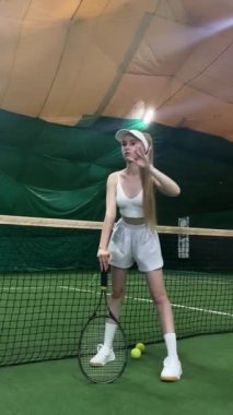 Genç bir atlet, kapalı bir tesiste tenis oynuyor. Odaklanma ve çevikliğini gösteriyor..