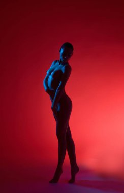 Kırmızı arka planda duran ve yana bakan üstsüz kadının tüm vücudu.