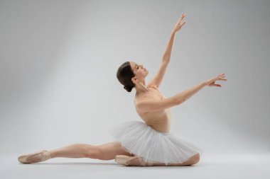 Bir dansçı zarifçe poz verir, minimalist bir stüdyoda duruşunu ve tekniğini sergiler. Atmosfer sanatçılık ve beceriyi vurguluyor..