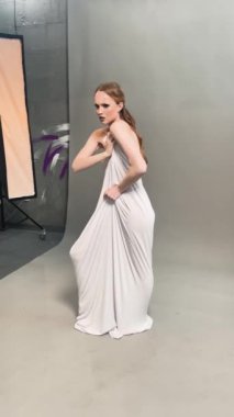 Şık gri elbiseli bir kadın stüdyoda poz veriyor, sanatsal moda teknikleri sergiliyor..