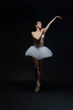 Bir balerin esnek ve zarif bir etekle esmer bir arka planda dans eder. Yetenekli hareketlerinin altını çizer..