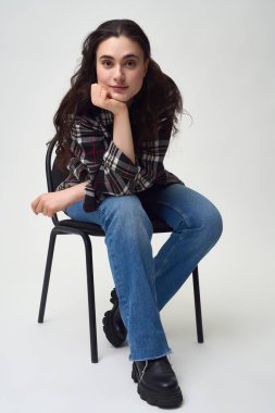 Moda kıyafetli, sandalyede oturan ve kameraya bakan genç bir kadın vücudu.