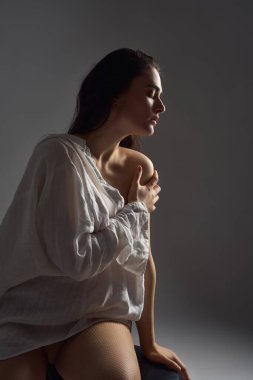 Gri arka planda duran şık iç çamaşırlı ve gömlekli şehvetli genç kadın modelinin yan görünüşü