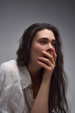 Kırış kırış gömlekli genç bir kadın model sandalyeye oturup başını arkaya yaslıyor ve gri arka planda gözlerini kapatıyor.