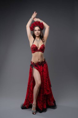 Zarif bir dansçı yeteneklerini, çiçeklerle süslenmiş muhteşem kırmızı bir elbiseyle sergiliyor. Tarafsız bir arkaplanda sanatsal bir performans sergiliyor..