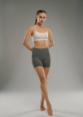 Genç bir kadın şık bir şekilde etek giyerek stüdyoda güçlü duruşunu sergiliyor. Arkaplan tarafsız, atletik figürlerini ve sakin tavırlarını geliştiriyor..