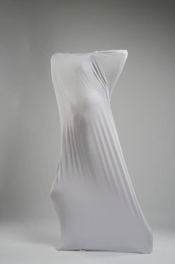 Geniş, minimalist bir stüdyoda, esnek beyaz bir kumaş ile meşgul olan bir insan ilginç şekiller ve gölgeler yaratır..