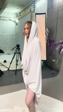 Beyaz elbiseli bir kadın moda atölyesinde poz veriyor, yaratıcılık ve zarafet sergiliyor..