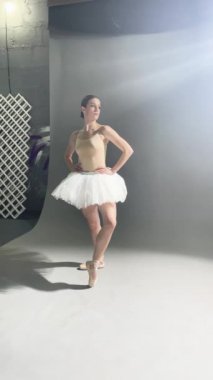 Bir kadın zarif bir şekilde bale kıyafeti içinde dans sanatını sergilerken sakin bir stüdyo ortamında poz veriyor..