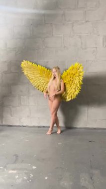 Bir kadın, yaratıcı bir stüdyo ortamında vücut sanatını ön plana çıkaran, kendine güvenen sarı kanatlarla poz verir..