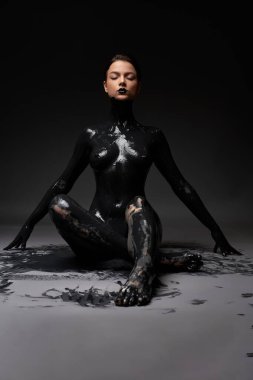 Siyah dudaklı, vücudu yağ boyasıyla kaplı, şehvetli, çıplak bir kadın vücudu. Karanlık odada, yerde zarifçe oturuyor.