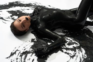 Çıplak kadın şamandırası beyaz zeminde boyalı seksi vücudu ile uzanıyor ve kameraya bakıyor.