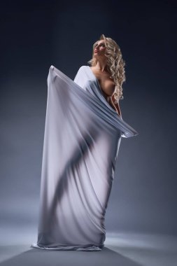 Uzun kıvırcık sarı saçlı, beyaz kumaşa sarılmış, koyu arkaplana bakan çekici, çıplak kadın mankenlerle dolu bir vücut.