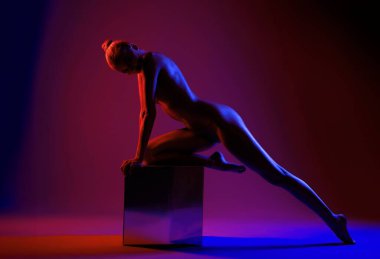 Bir model canlı mor ve kırmızı ışıkla yıkanmış yansıtıcı bir yüzeyde dinamik bir duruş sergiler..