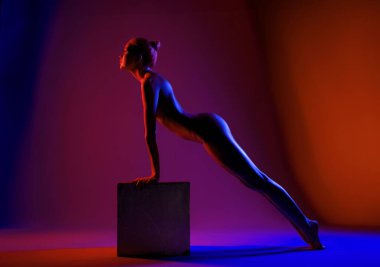 Bir kadın, canlı kırmızı ve mavi ışıkla aydınlatılan bir küpün üzerinde şınav çeker, şeklini ve gücünü gösterir..