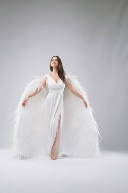 A woman in a white dress with large white feathered wings stands on a white background, looking up. clipart