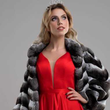 Bir model dikkat çekici kırmızı bir elbise ve lüks bir kürk manto giyer. Tacı takarken zarafet ve duruş sergiler..