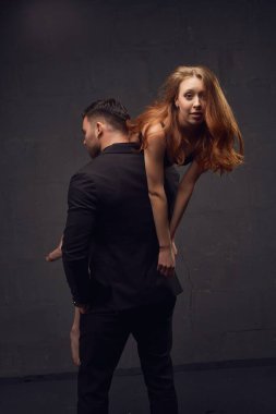 Siyah takım elbiseli meçhul erkek stüdyoda siyah arka planda güzel bir kız arkadaşı omuzlarında taşıyor.