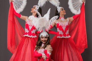 Three performers showcase an elaborate dance routine, wearing stunning red costumes adorned with feathers at a lively celebration. clipart