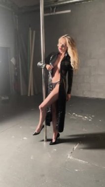 Bir kadın bir direğin yanında çıplak ve üstsüz poz verirken güzelliğini ve özgüvenini sergiler..